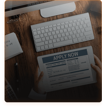 Job application desk with computer and tablet showing APPLY NOW